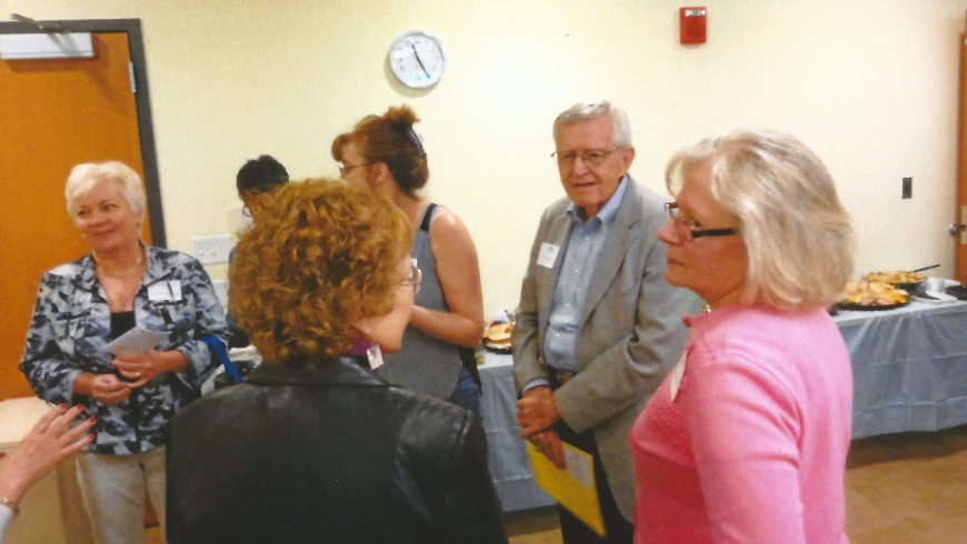 Two women have a conversation with their backs to the camera. A man in front of them faces the camera.