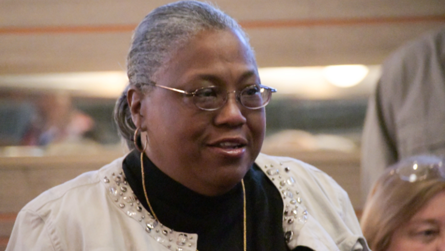 Up-close image of a woman in a white sweater and black shirt. The woman is lookin to the right of the camera.