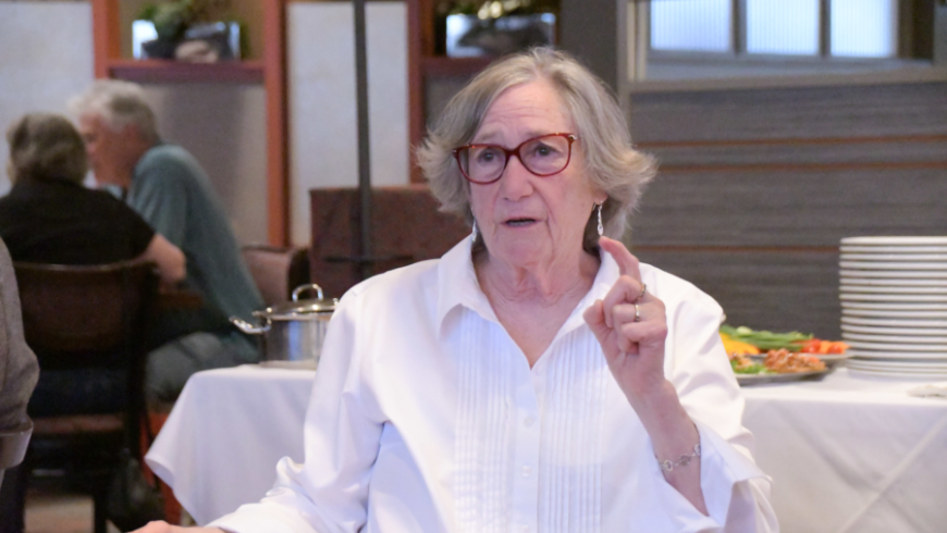 A woman wearing a white shirt speaks while sitting down