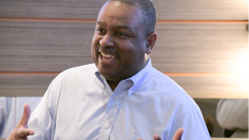 A man in a white shirt stands and speaks. 