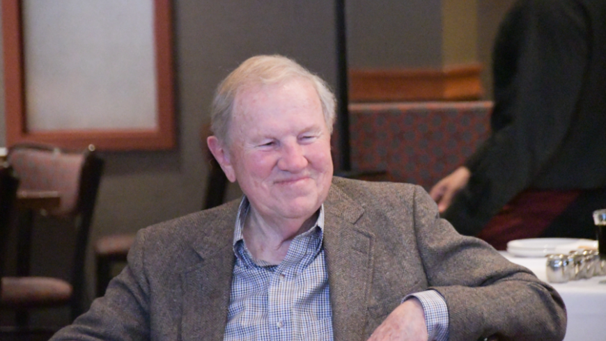 A man wearing a gray suit jacket sits and looks to the right of the camera.