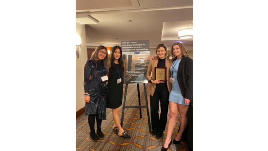 Four women, including members of the Opendak Lab team, pose for a photo. At the center is an easel displaying information about the conference.  