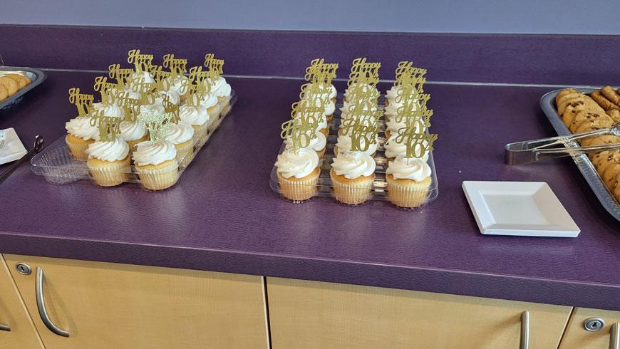 Two trays of cupcakes with 10th anniversary toppers sit on a counter.
