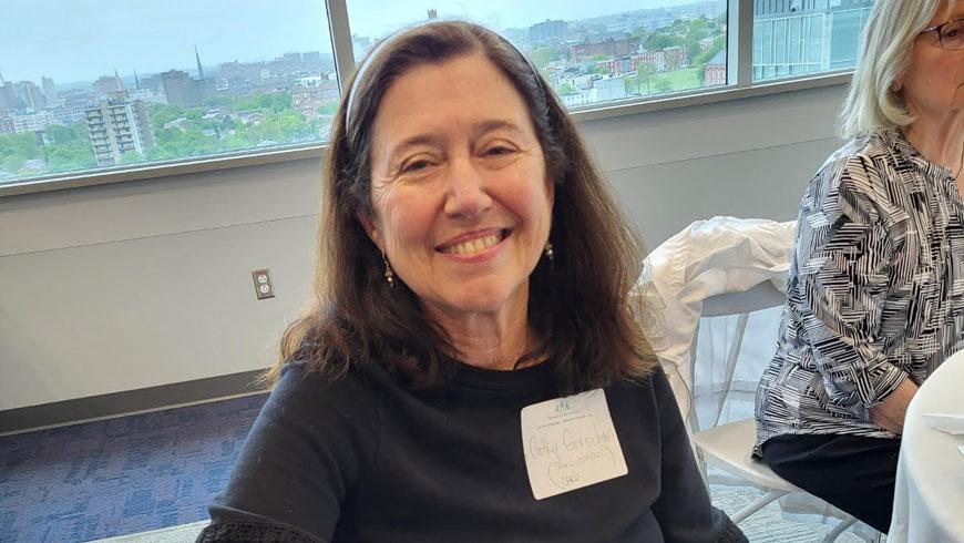 A woman seated at a table smiles at the camera.