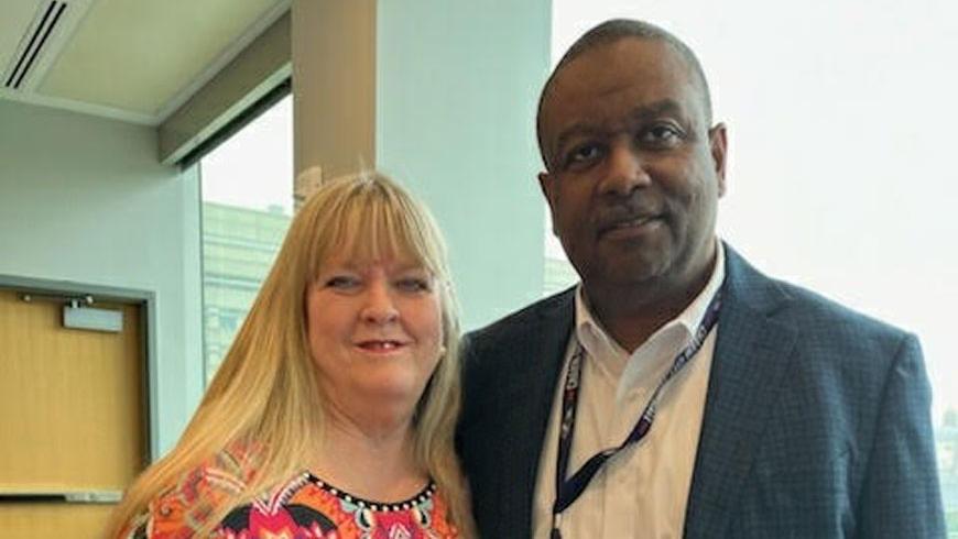 A man and a woman stand next to each other and smile for a photo.