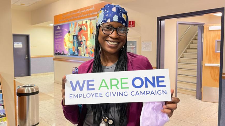 A woman smiles while holding a We Are One sign