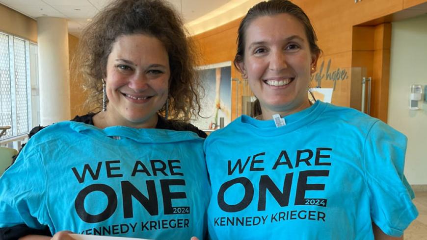 Two women smile wearing We Are One t-shirts.