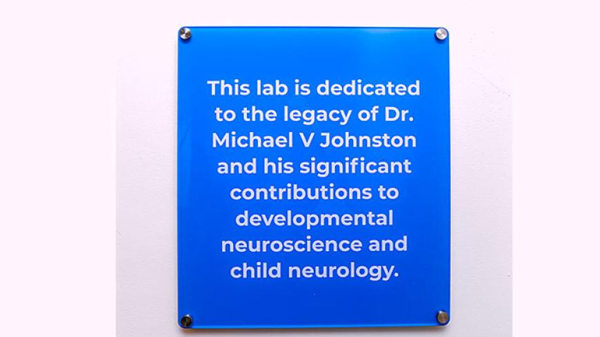 A blue sign with white text that reads, This lab is dedicated to the memory of Dr. Michael V. Johnston and his significant contributions to developmental neuroscience and child neurology.