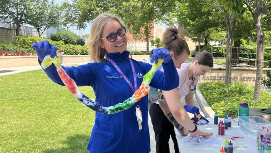 Dr. Cristina Sadowsky smiles while holding a painted t-shirt in Kennedy Krieger's therapy garden.