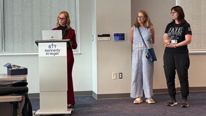Dr. Cristina Sadowsky speaks at the rends in Spinal Cord Rehabilitation Symposium. Two women are seen standing off to her left side as she speaks.