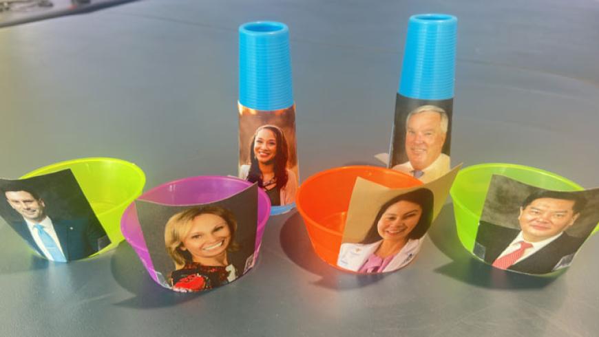 Six plastic cups, each with an ICSCI staff member's headshot taped to them. The cups were made during the Olympics event.