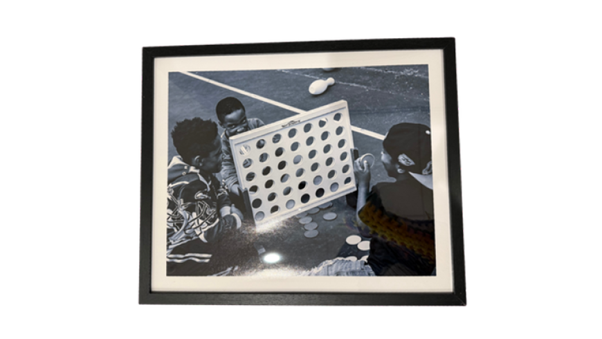 Black‑and‑white framed photo of three children playing a large Connect Four-style game on a playground