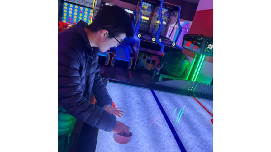 A CORE Foundations participant plays air hockey in an arcade.