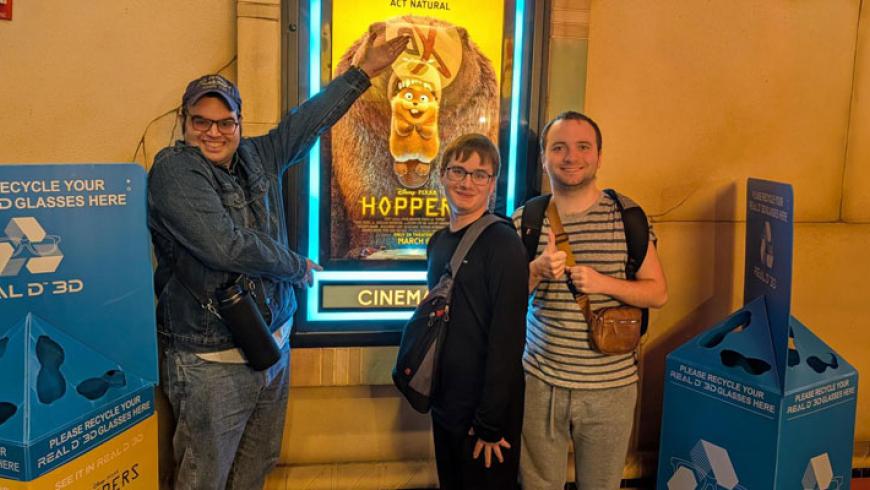 Three CORE Foundations participants smile while standing in front of a movie poster.