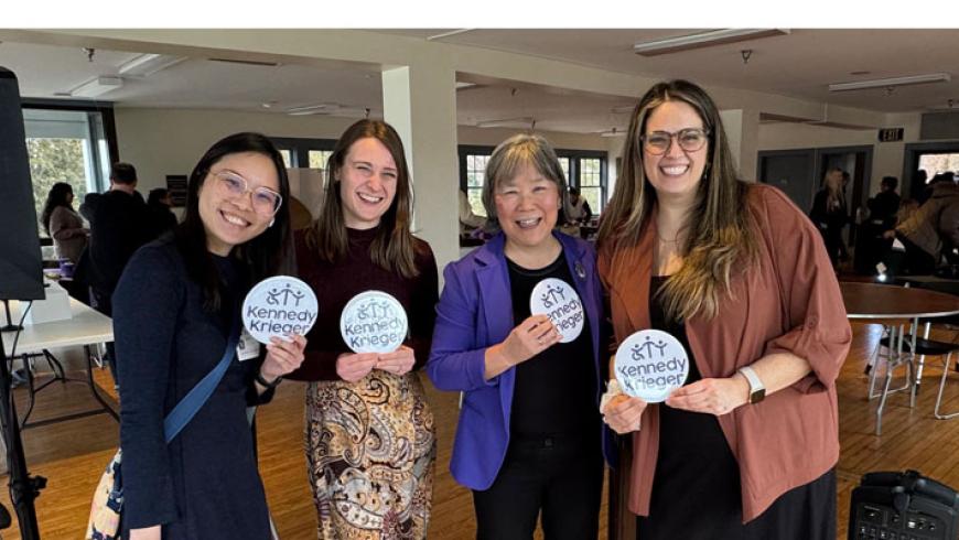 Four women smile while holding items featuring Kennedy Krieger's logo.