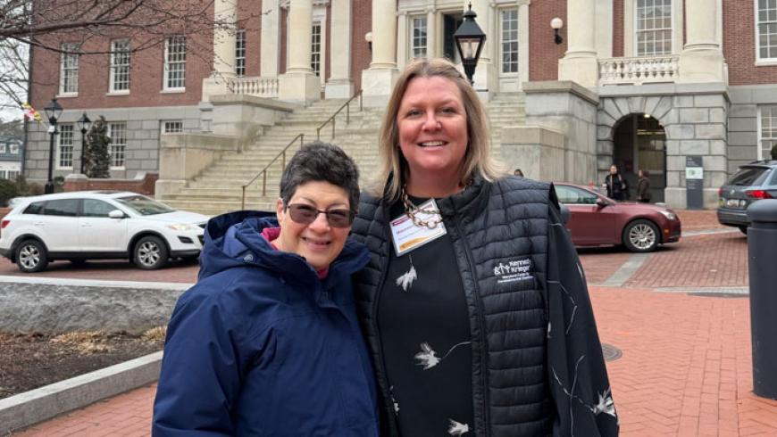 Two women smile while standing in front of the Maryland State House.