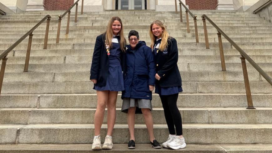 Three women smile while standing on the steps of the Maryland State House.