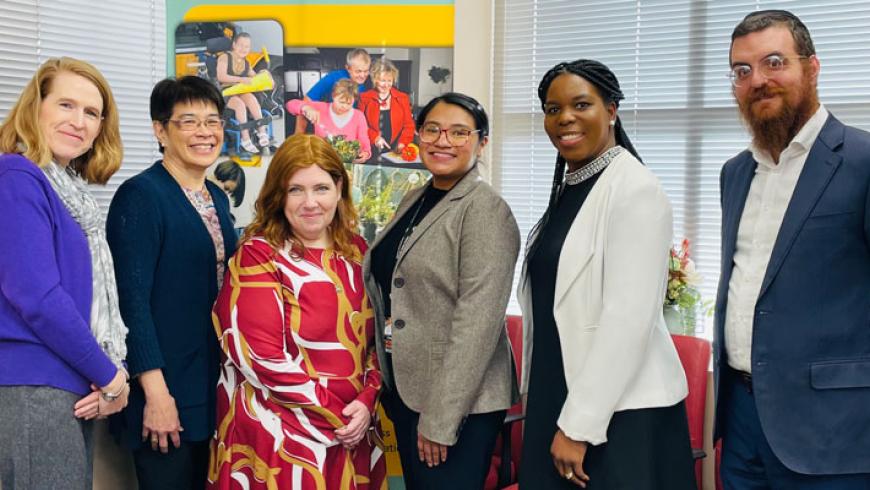Six people smile as they stand in front of an MCDD banner.