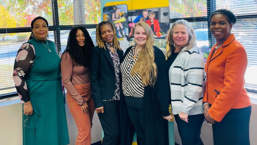 Six people stand in front of a banner and smile.