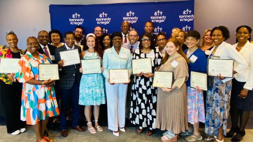 Faith Community Learning Collaborative Disability Inclusion Ambassadors stand in front of a Kennedy Krieger banner. Some of them are holding certificates.