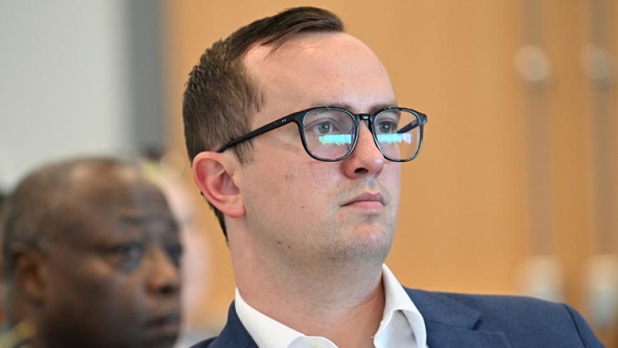 A man sitting among other conference attendees listens to a presentation.