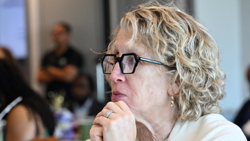 A woman rests her hands near her face while listening to a conference presentation.