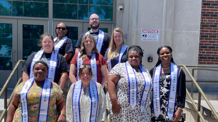 Eight people wearing Family Engagement and Champion stoles pose on the steps outside a building entrance during a group photo.