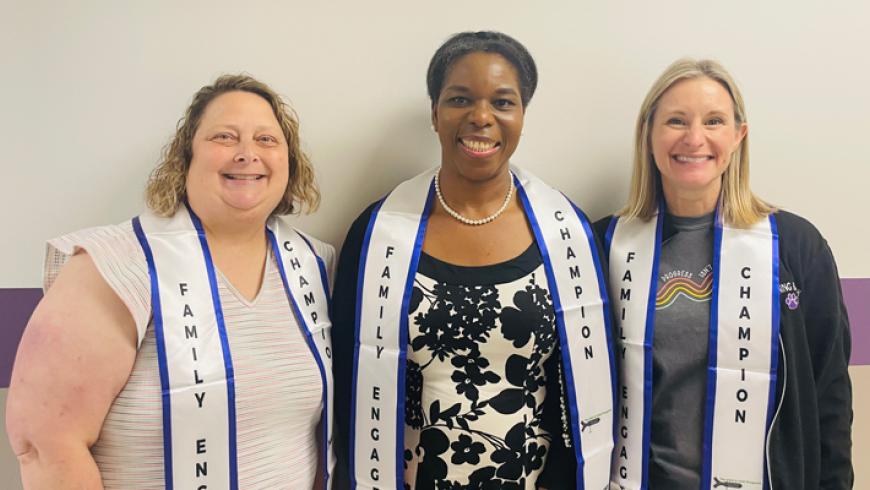 Three people wearing Family Engagement and Champion stoles stand side by side against a wall with a purple stripe, posing for a group photo.