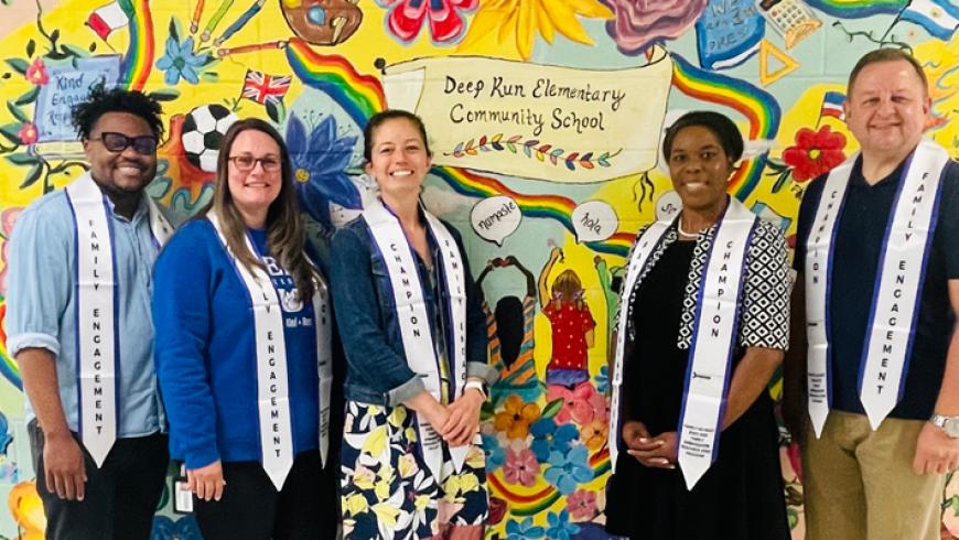 Five people wearing “Family Engagement” and “Champion” stoles stand in front of a colorful mural at Deep Run Elementary Community School.